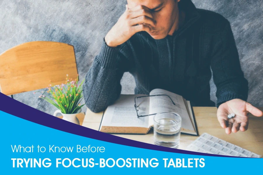 Man contemplating focus-boosting tablets while studying with books and water on the table.